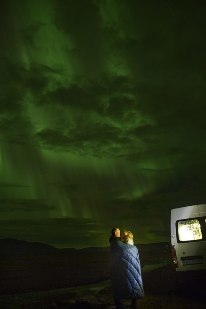 Couple cuddled up watching Northern Lights off side of road in North Iceland