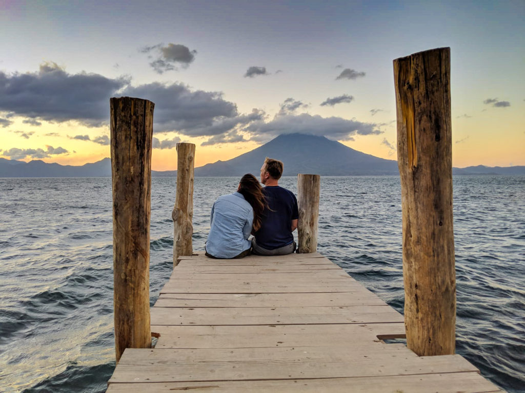 Couple sitting on dock watching sunrise from Santa Cruz La Laguna, Lake Atitlan, Guatemala