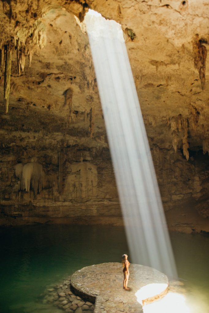 Woman standing on platform at cenote Suytan with sunbeam, Valladolid, Mexico