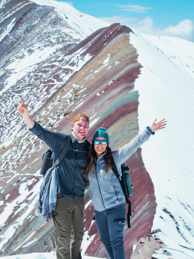 Man and woman with outstretched arms on top of Rainbow Mountain, Vinicunca Peru
