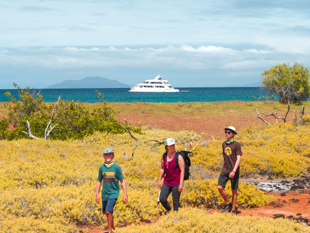 Family hiking on island with Galagents cruise ship in background, Galapagos Islands, Ecuador