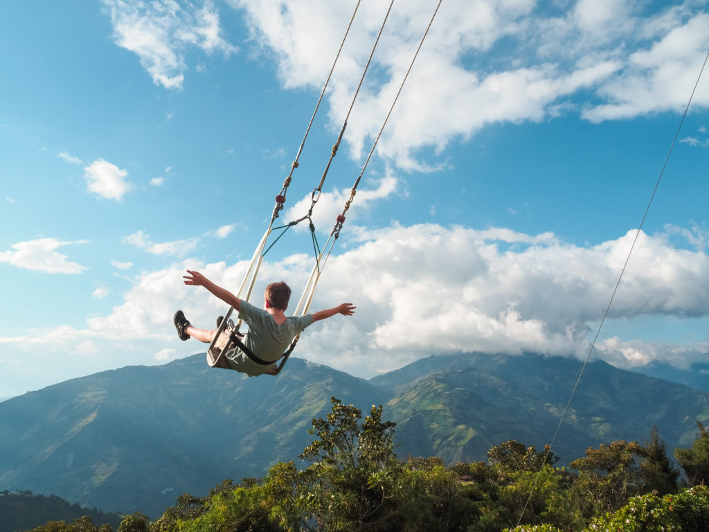Kid swinging on swing with arms outstretched at Casa del Arbol, Banos, Ecuador