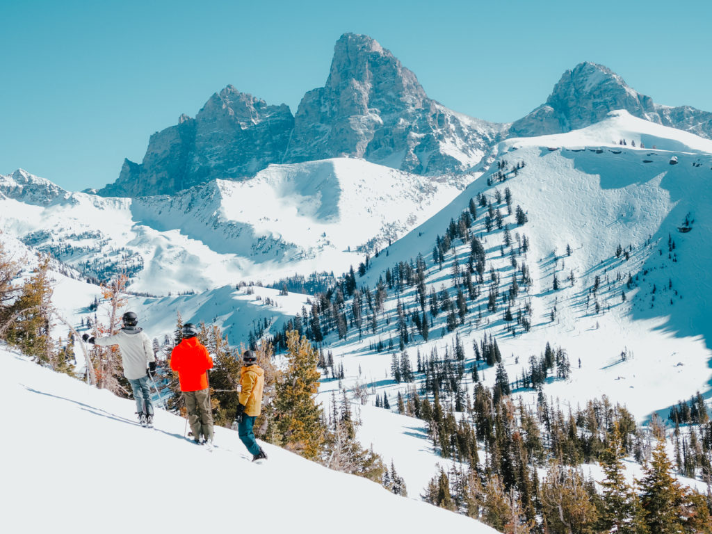3 skiers stand looking out to the Teton Mountain range from Grand Targhee Ski Resort in Idaho